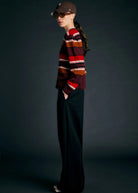 Person wearing a striped sweater and dark pants against a dark background