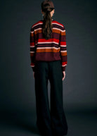 Person wearing a striped sweater and dark pants against a dark background