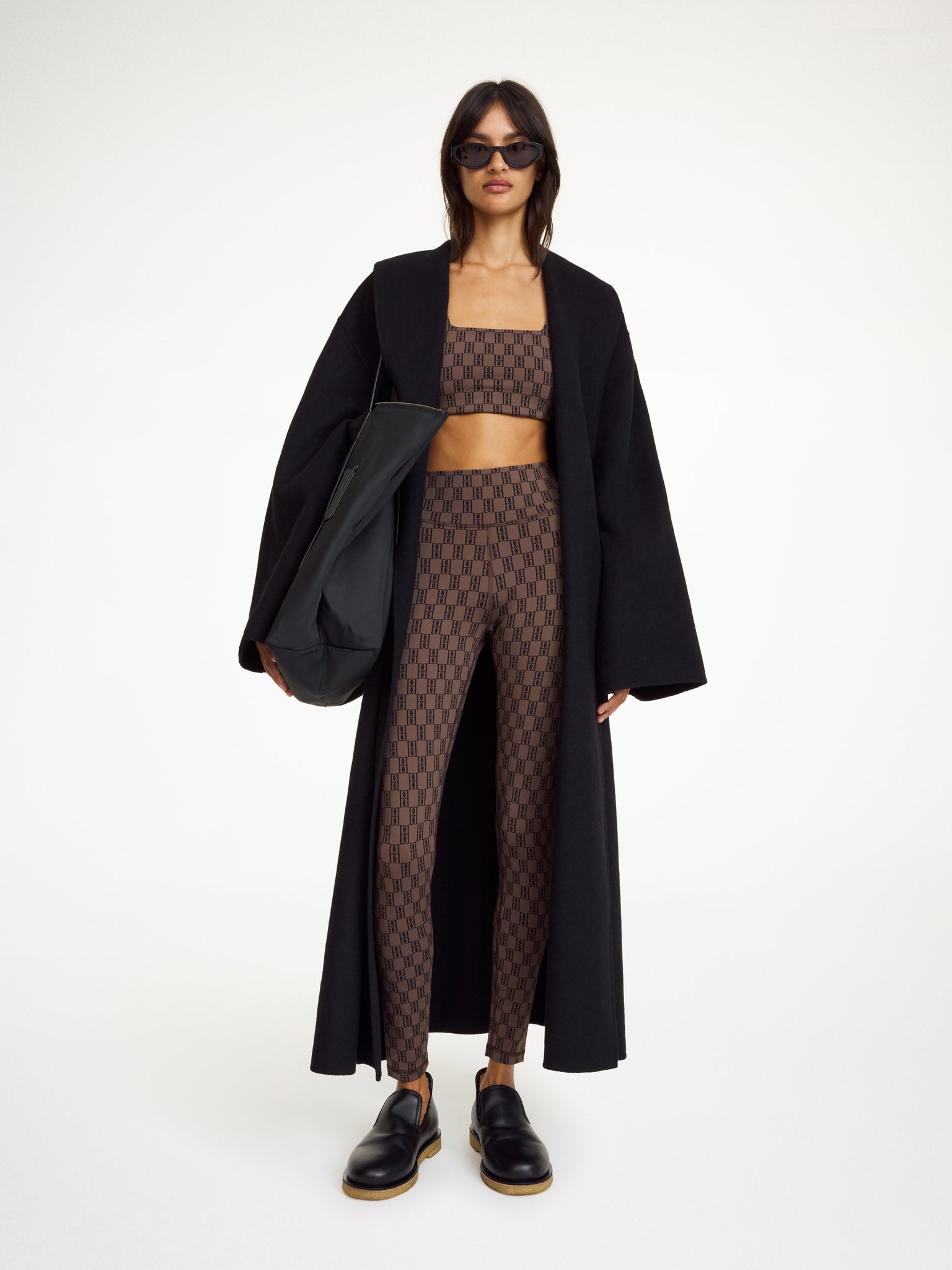 Woman wearing a black coat, patterned top, and leggings on a white background