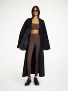 Woman wearing a black coat, patterned top, and leggings on a white background