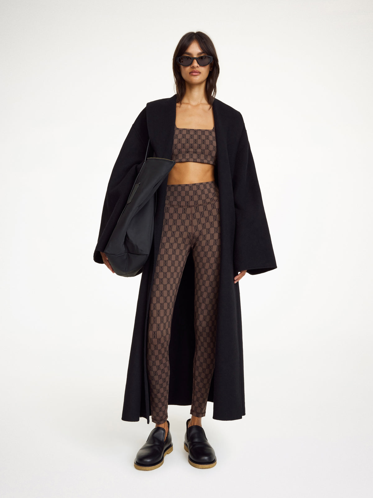 Woman wearing a black coat, patterned top, and leggings on a white background
