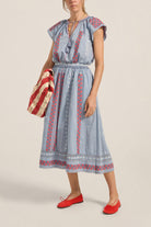 Woman wearing a blue dress with red patterns and holding a striped bag on a beige background