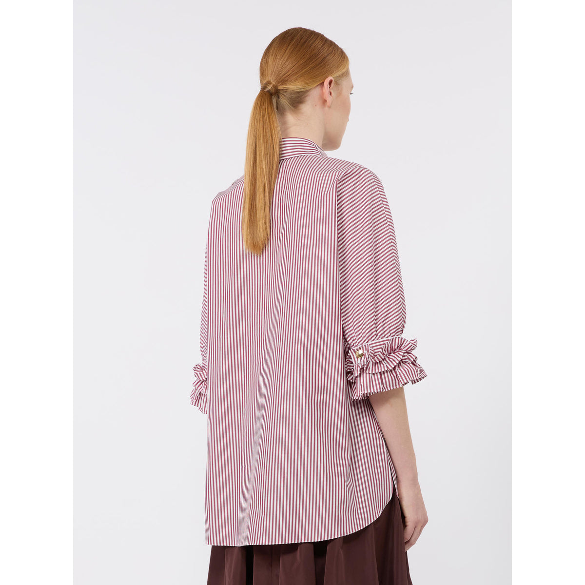 Person wearing a pink and white striped shirt with ruffled sleeves on a white background
