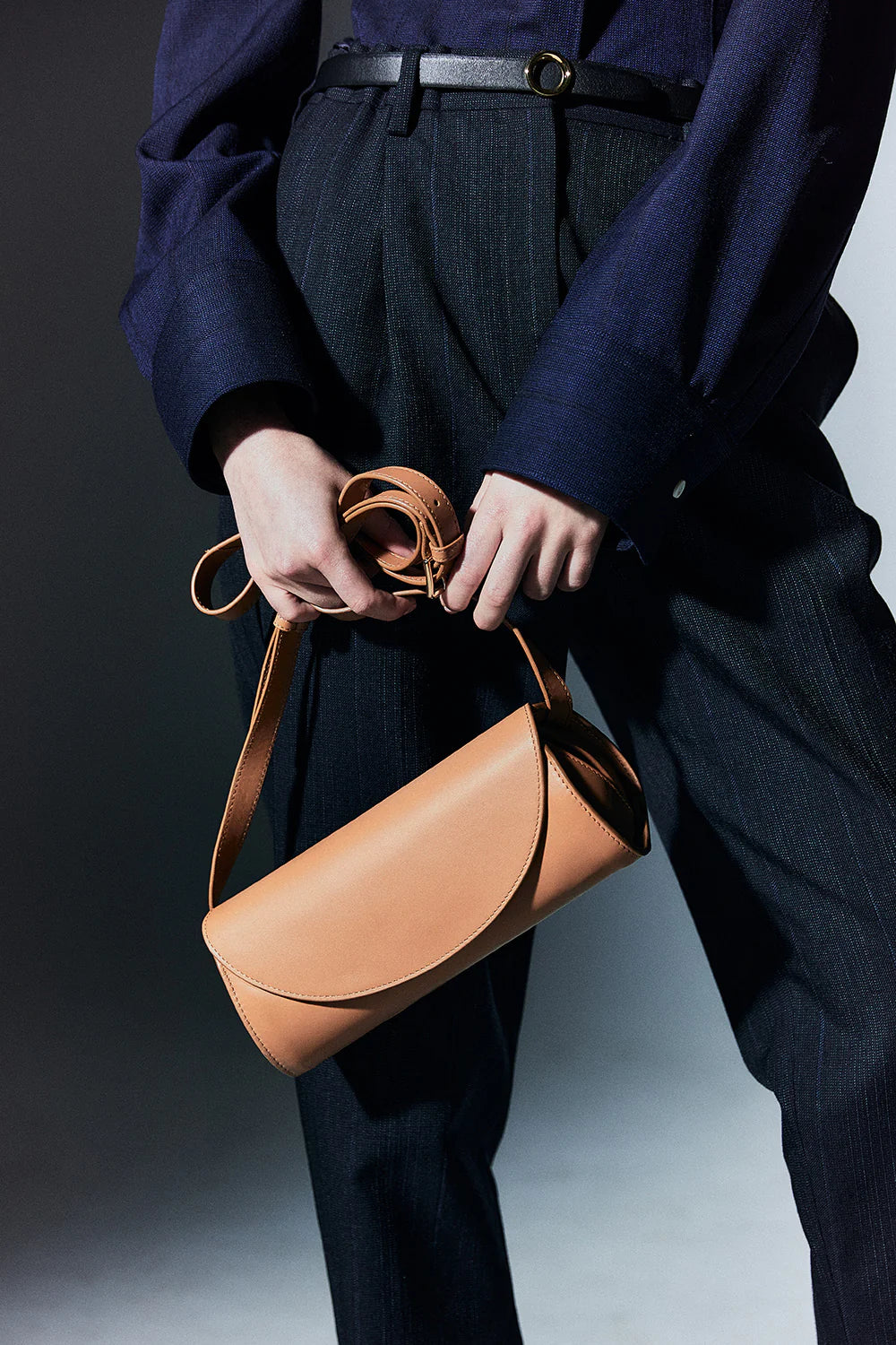 Person holding a tan handbag against a neutral background