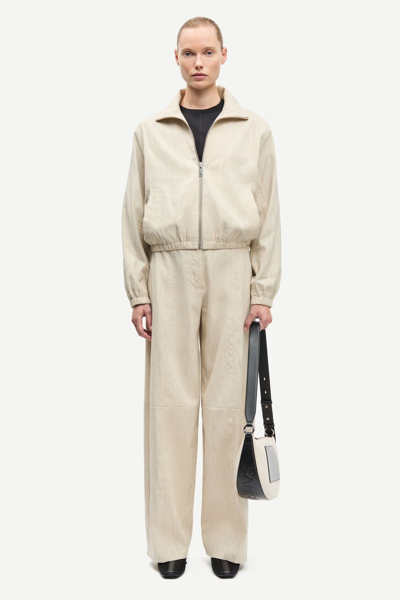 Person wearing a beige tracksuit holding a black bag on a white background