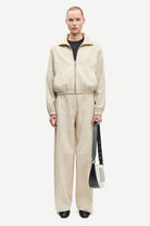 Person wearing a beige tracksuit holding a black bag on a white background