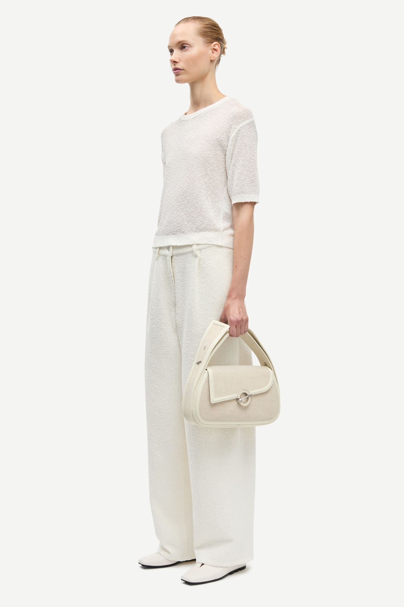 Woman holding a cream handbag against a white background