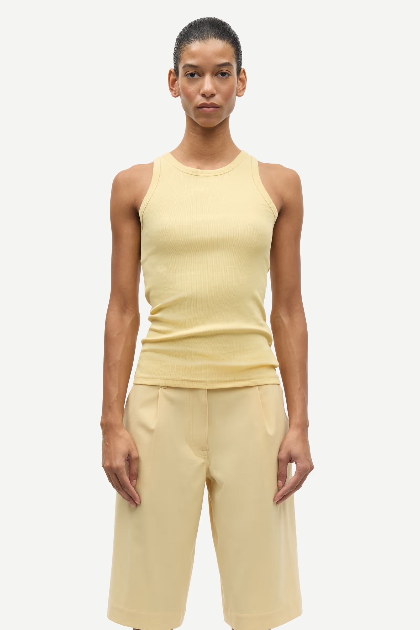 Person wearing a beige tank top and shorts on a white background