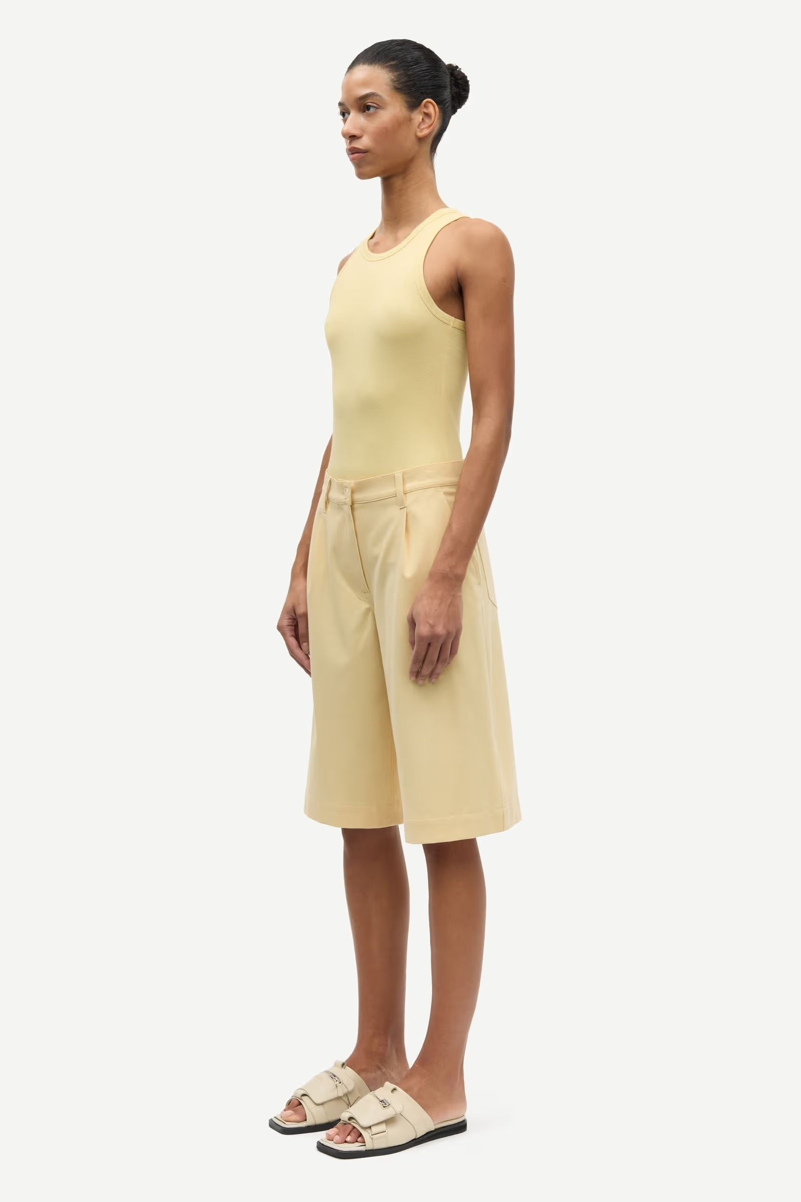 Woman wearing a yellow sleeveless top and shorts on a white background