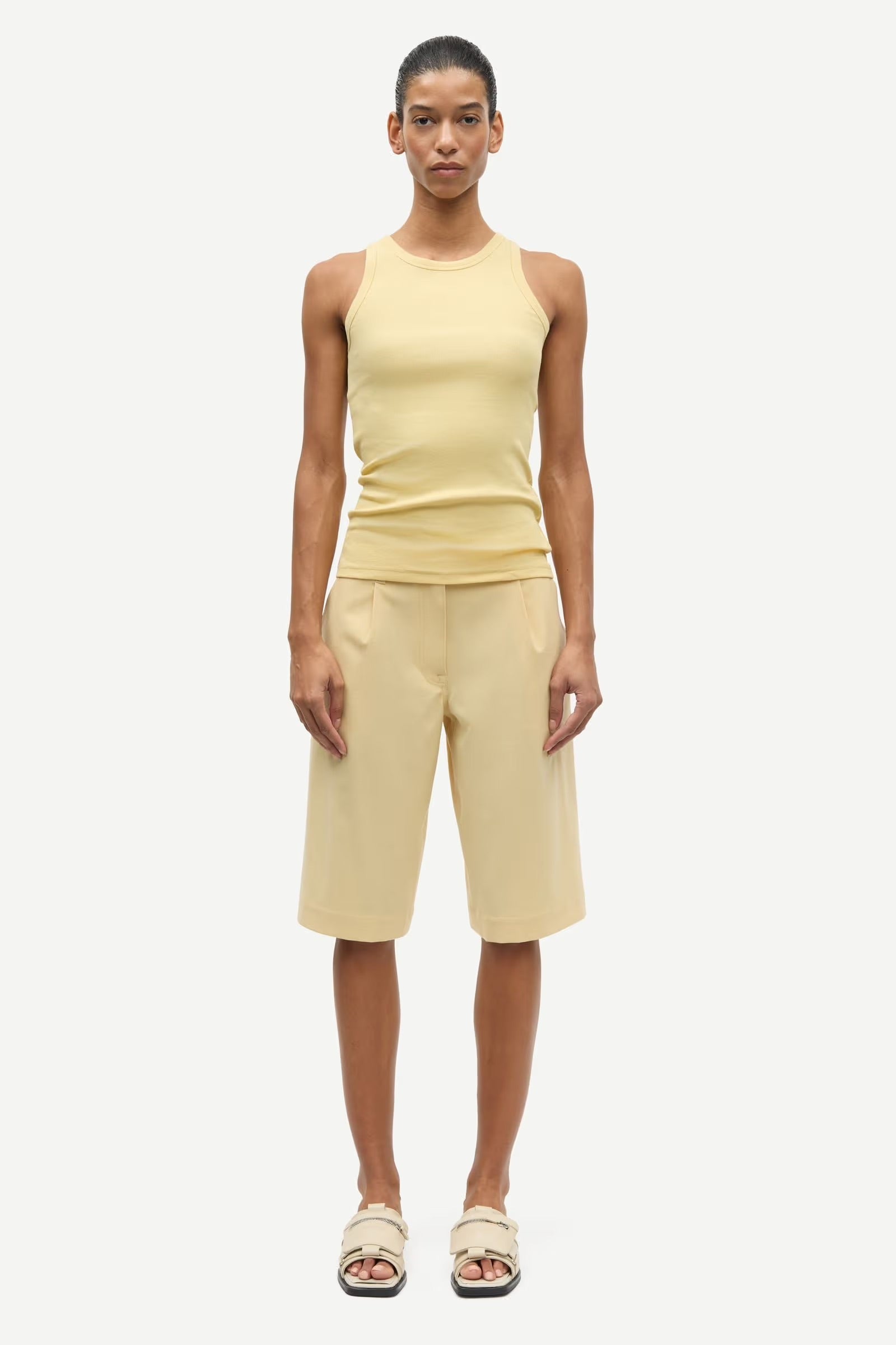 Woman wearing a yellow sleeveless top and shorts on a white background