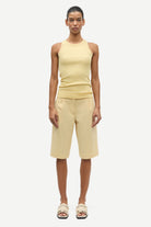 Woman wearing a yellow sleeveless top and shorts on a white background