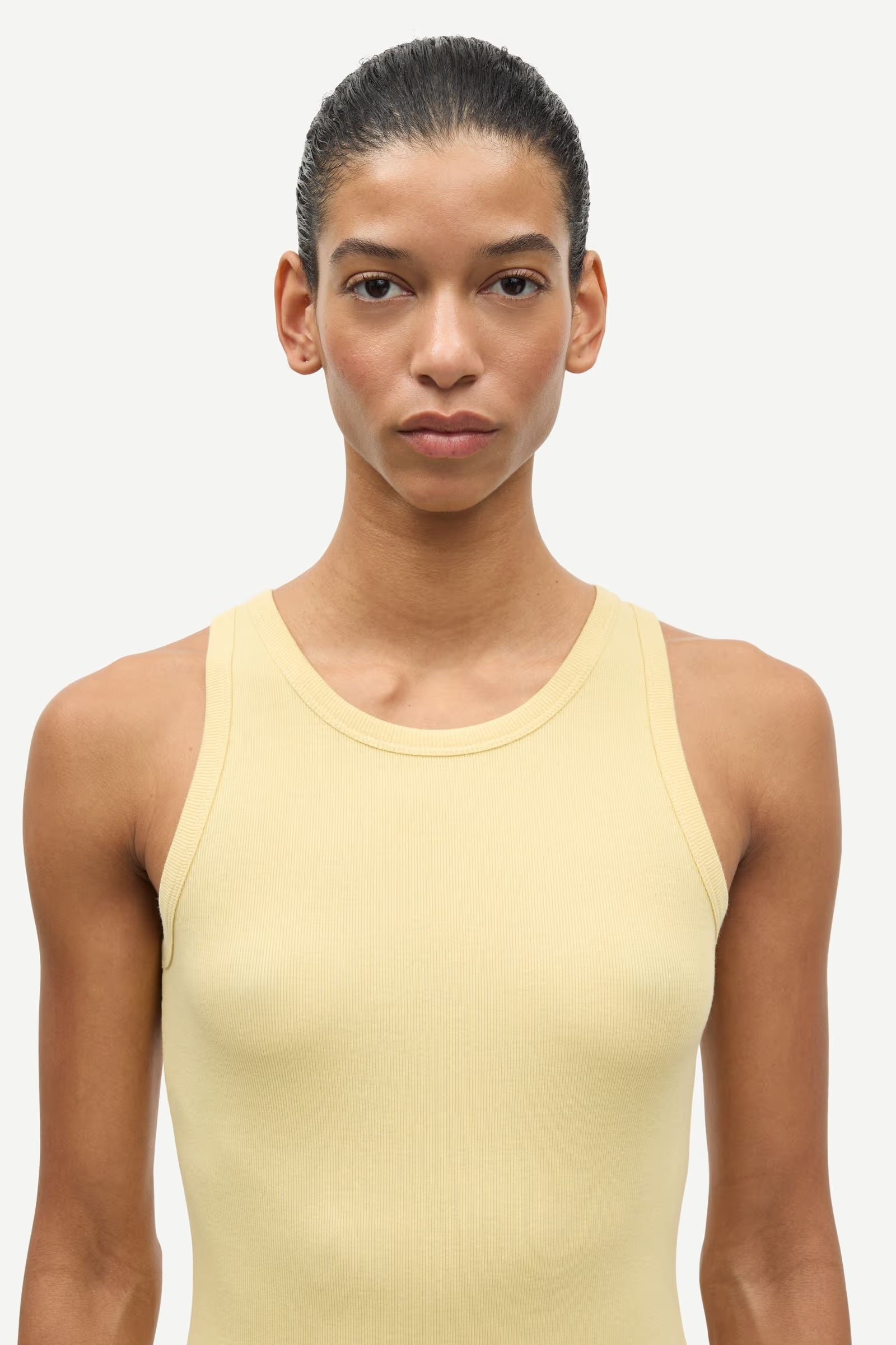 Woman wearing a light yellow tank top against a white background
