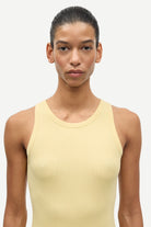 Woman wearing a light yellow tank top against a white background