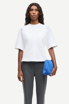 Woman wearing a white top and gray pants, holding a blue clutch against a white background