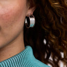 Close-up of a person wearing a silver hoop earring with a blurred background