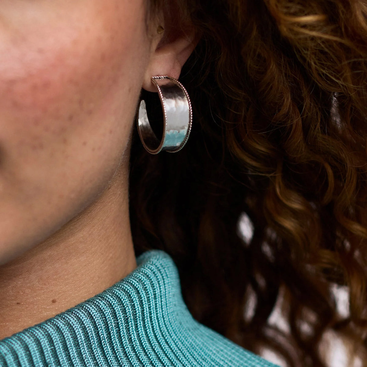 Close-up of a person wearing a silver hoop earring with a blurred background