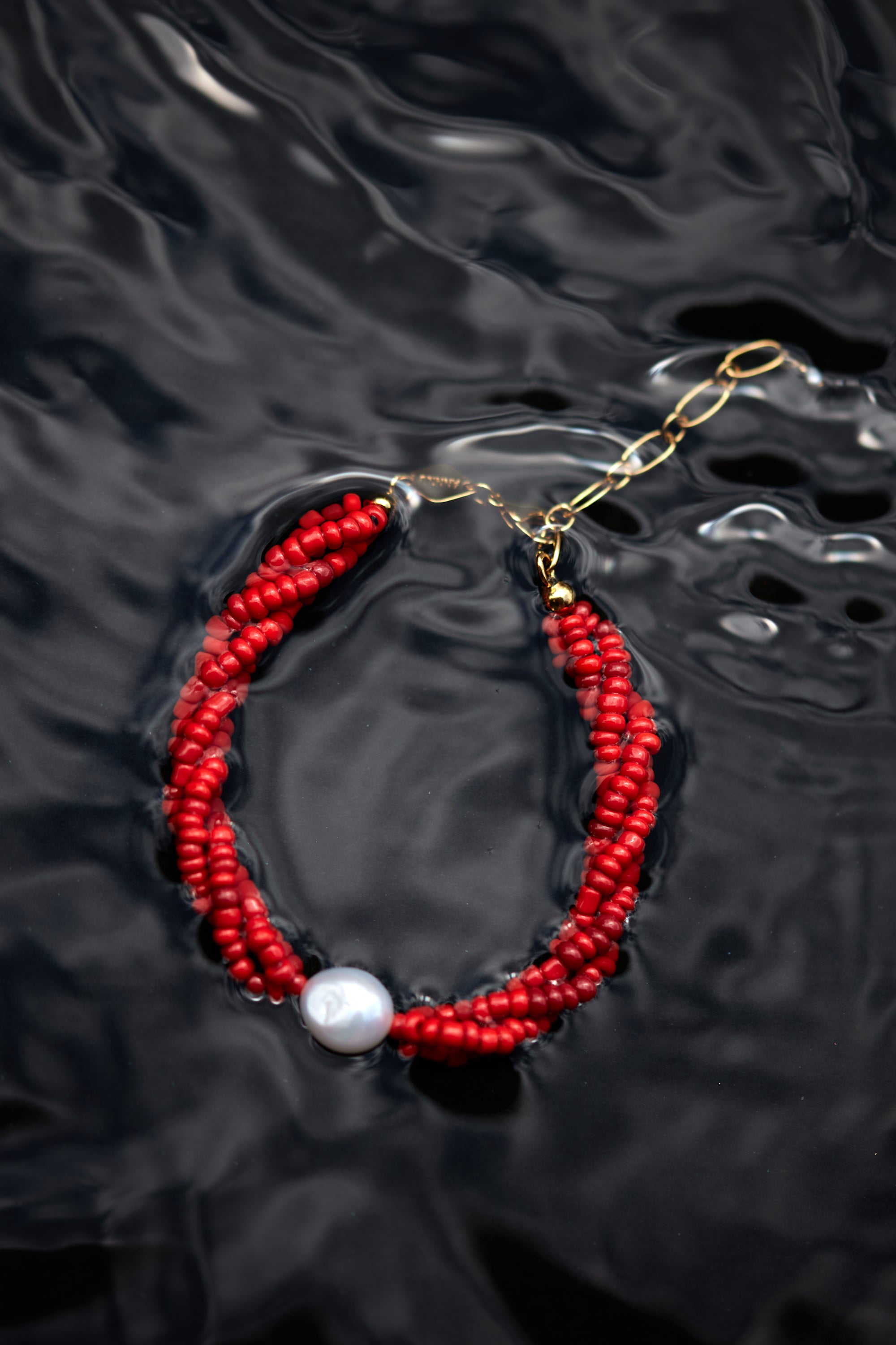 Red beaded bracelet with a pearl on a dark, textured surface