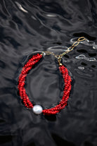 Red beaded bracelet with a pearl on a dark, textured surface