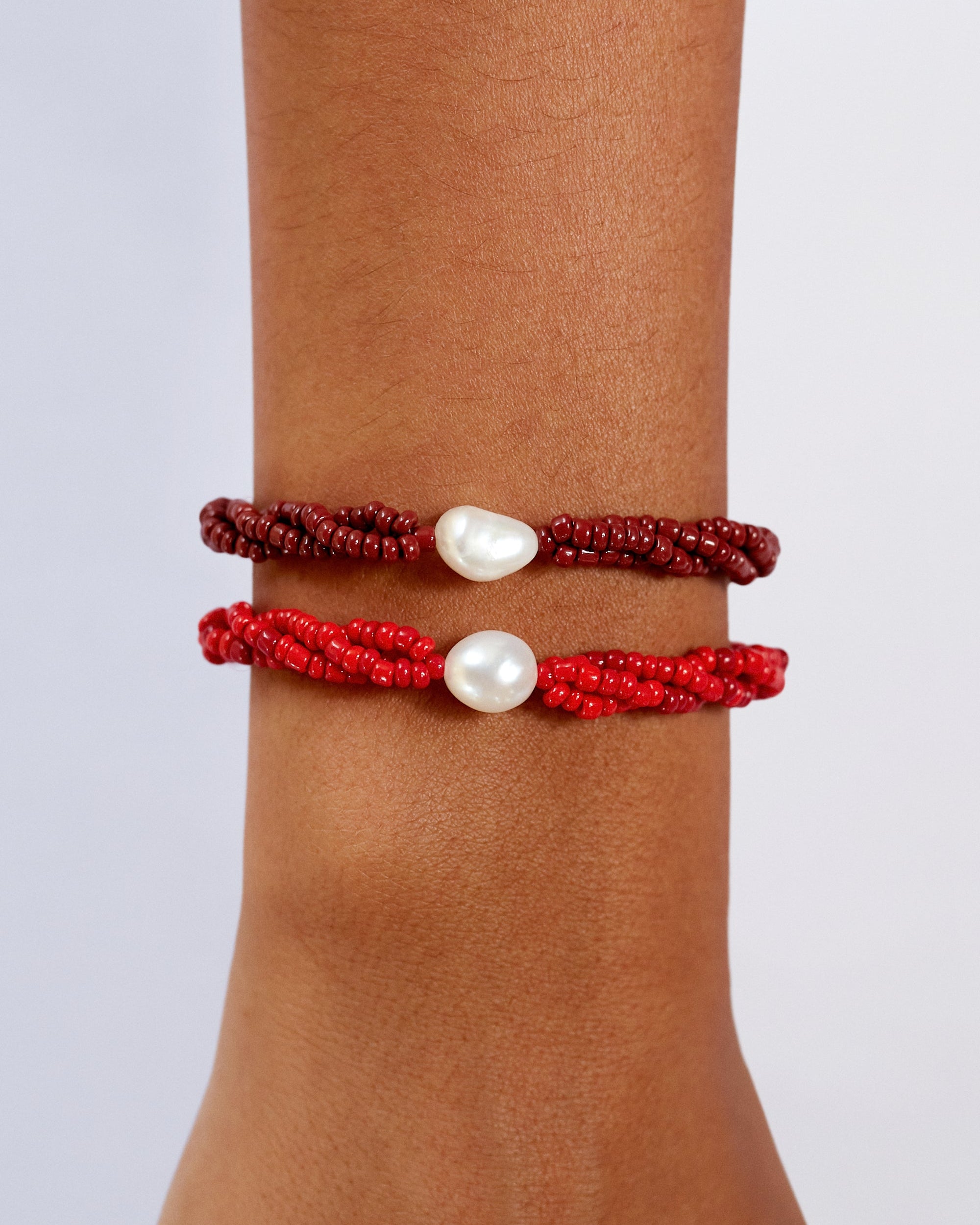 Two red beaded bracelets with white pearls on a wrist against a light gray background