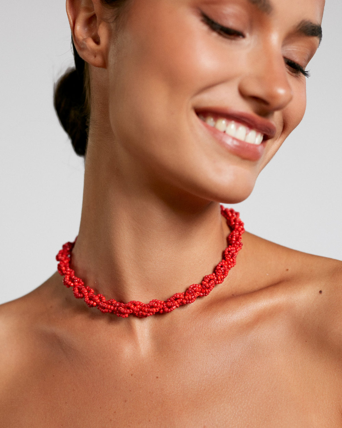 Woman wearing a red necklace against a neutral background