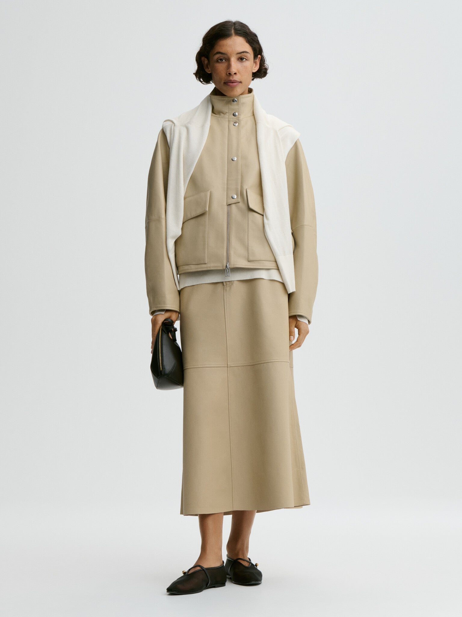 Woman wearing a beige outfit with a white scarf on a light gray background