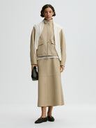 Woman wearing a beige outfit with a white scarf on a light gray background