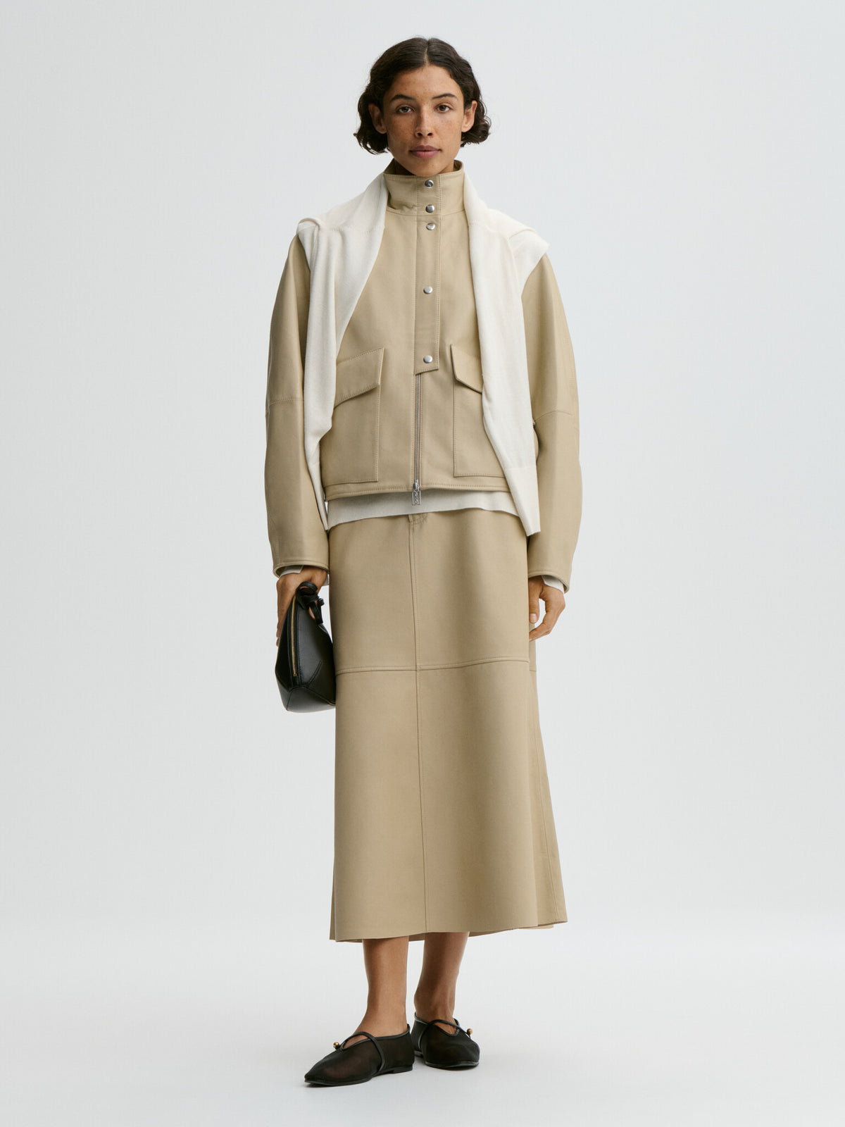 Woman wearing a beige outfit with a white scarf on a light gray background