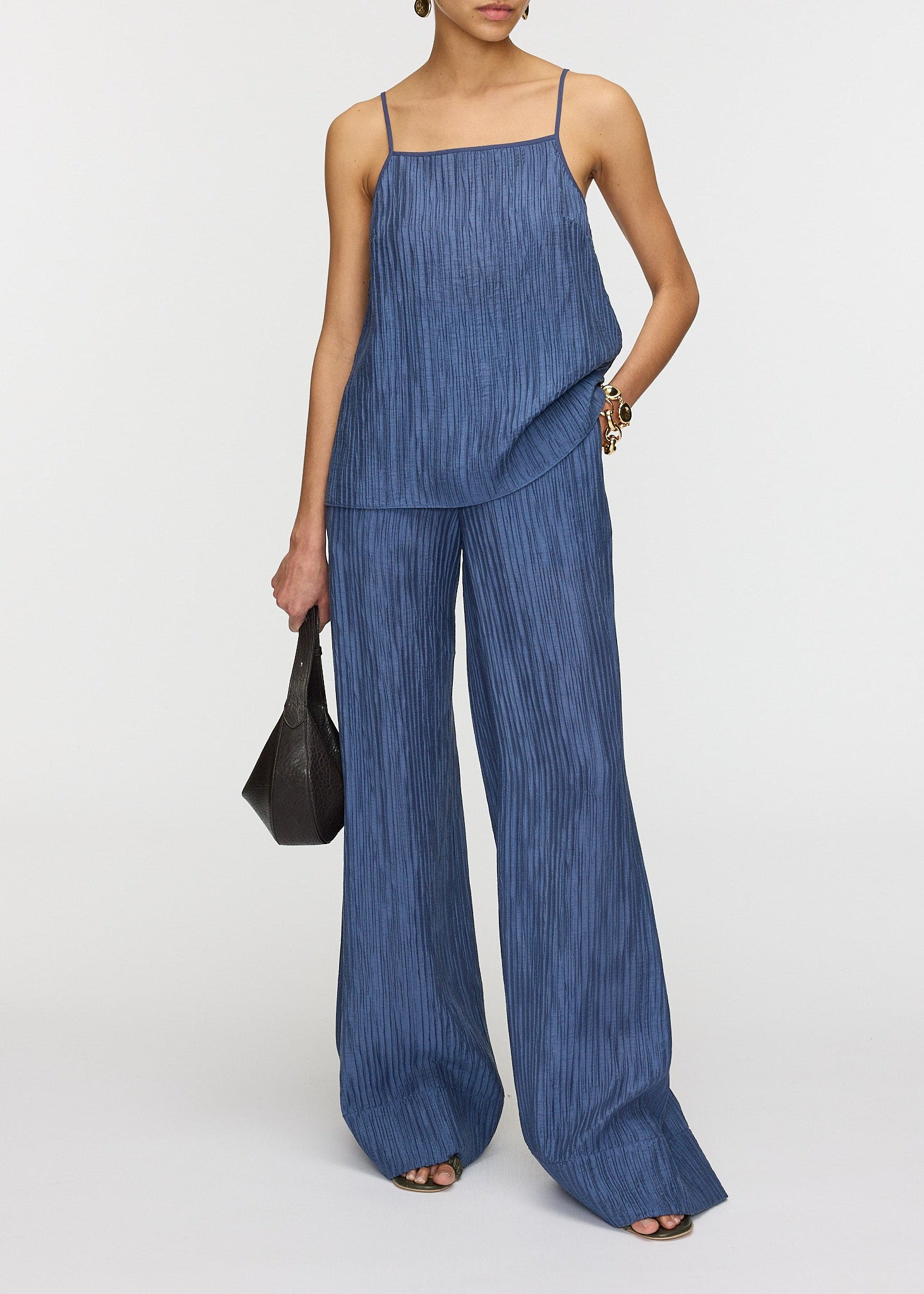 Woman wearing a blue textured suit holding a black handbag on a white background