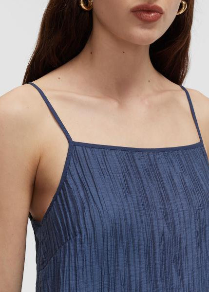Close-up of a woman wearing a textured slate blue spaghetti-strap top against a light gray background.