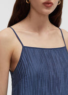 Close-up of a woman wearing a textured slate blue spaghetti-strap top against a light gray background.