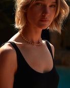 Woman wearing a black top and gold necklace with a blurred background