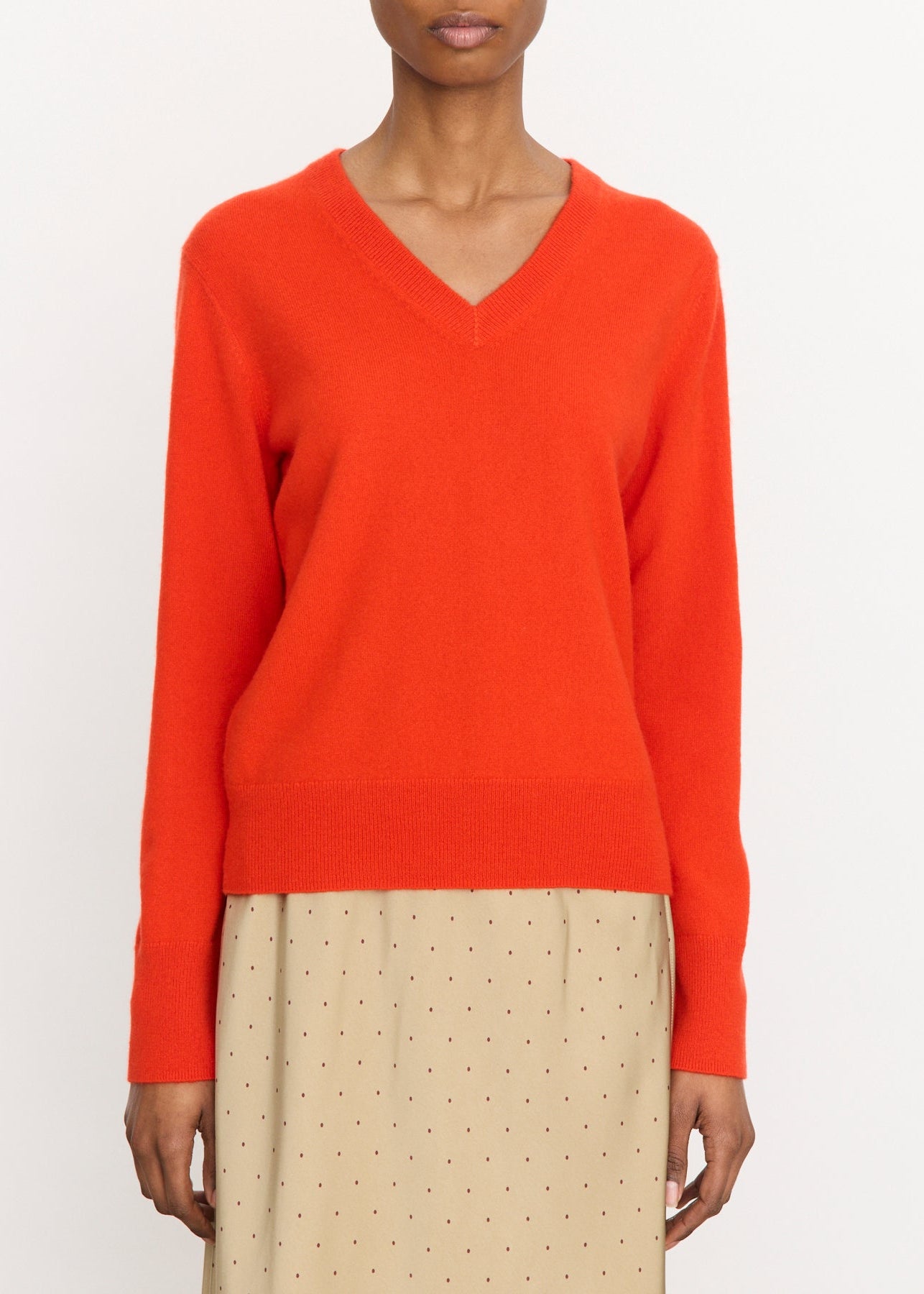 Person wearing a bright orange sweater with beige pants on a white background