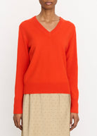 Person wearing a bright orange sweater with beige pants on a white background