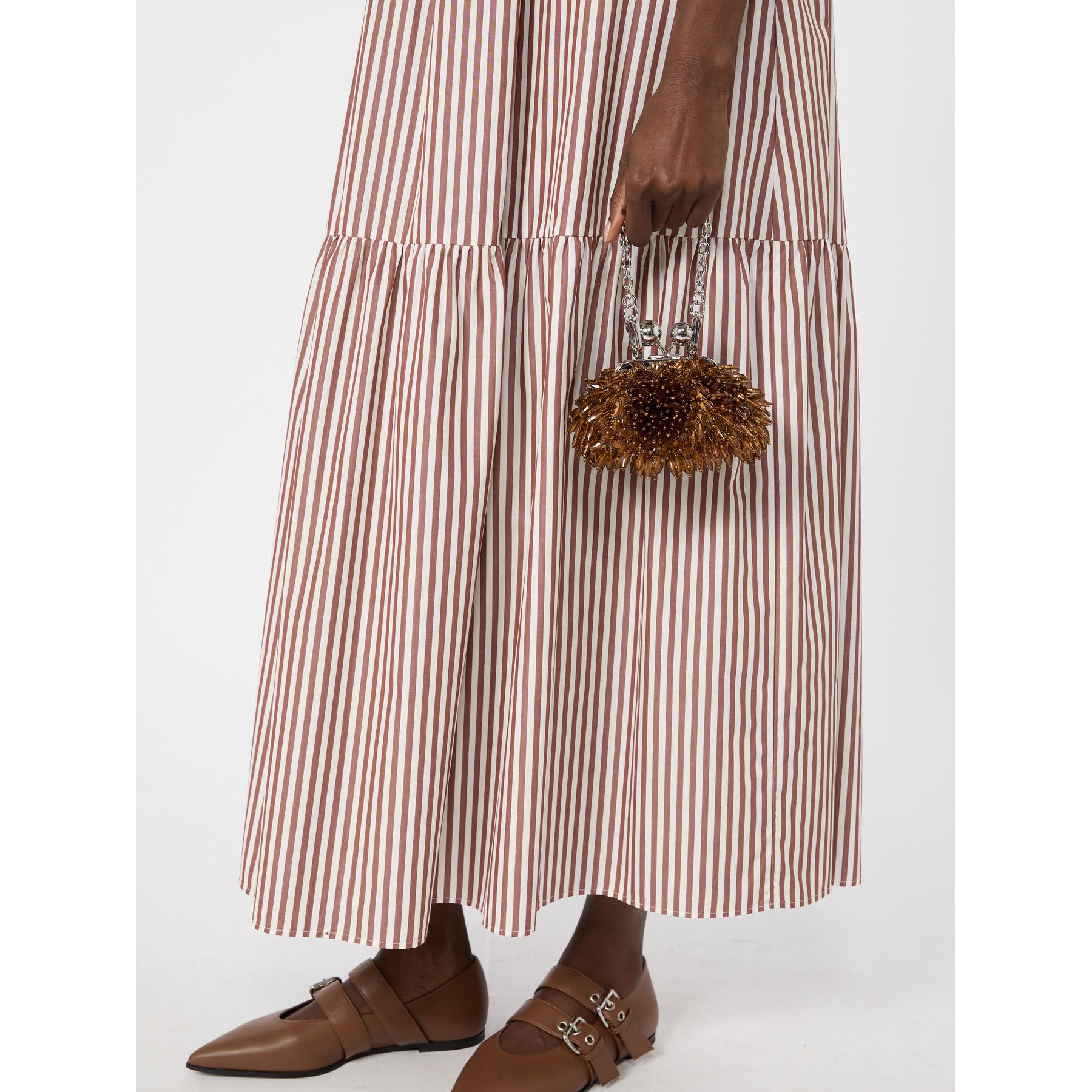 Person wearing a long brown and white striped dress holding a small handbag on a white background
