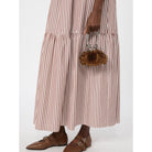 Person wearing a long brown and white striped dress holding a small handbag on a white background