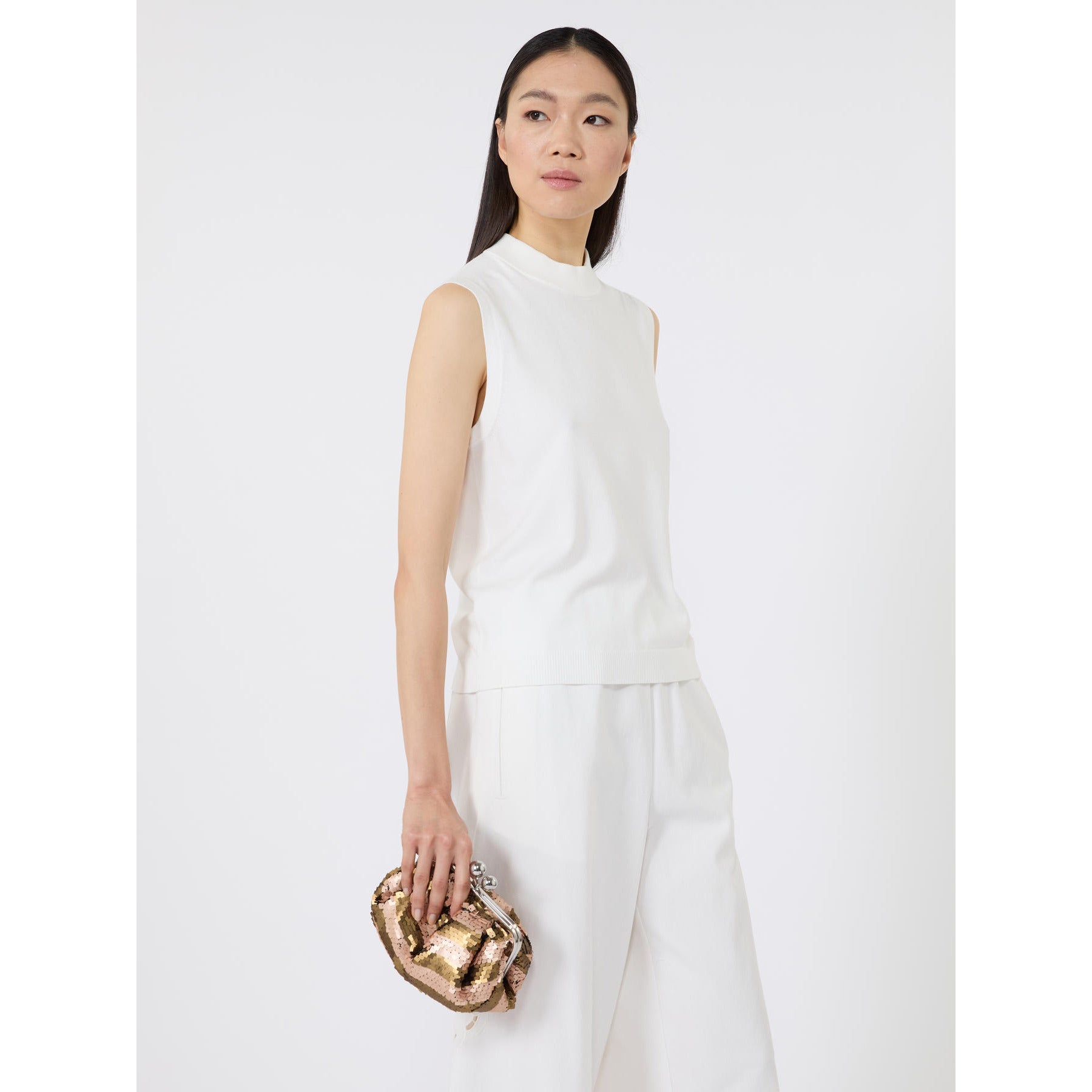Woman in a white outfit holding a gold clutch against a white background