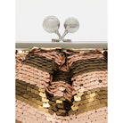 Sequined fabric with a gradient of gold, bronze, and rose gold colors, with a branded lamp in the background.