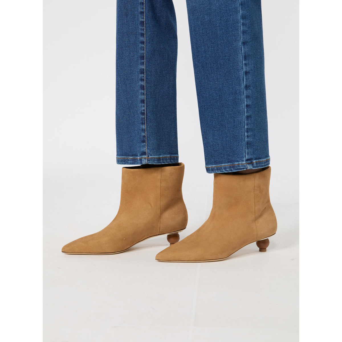 Tan ankle boots worn with blue jeans on a white background