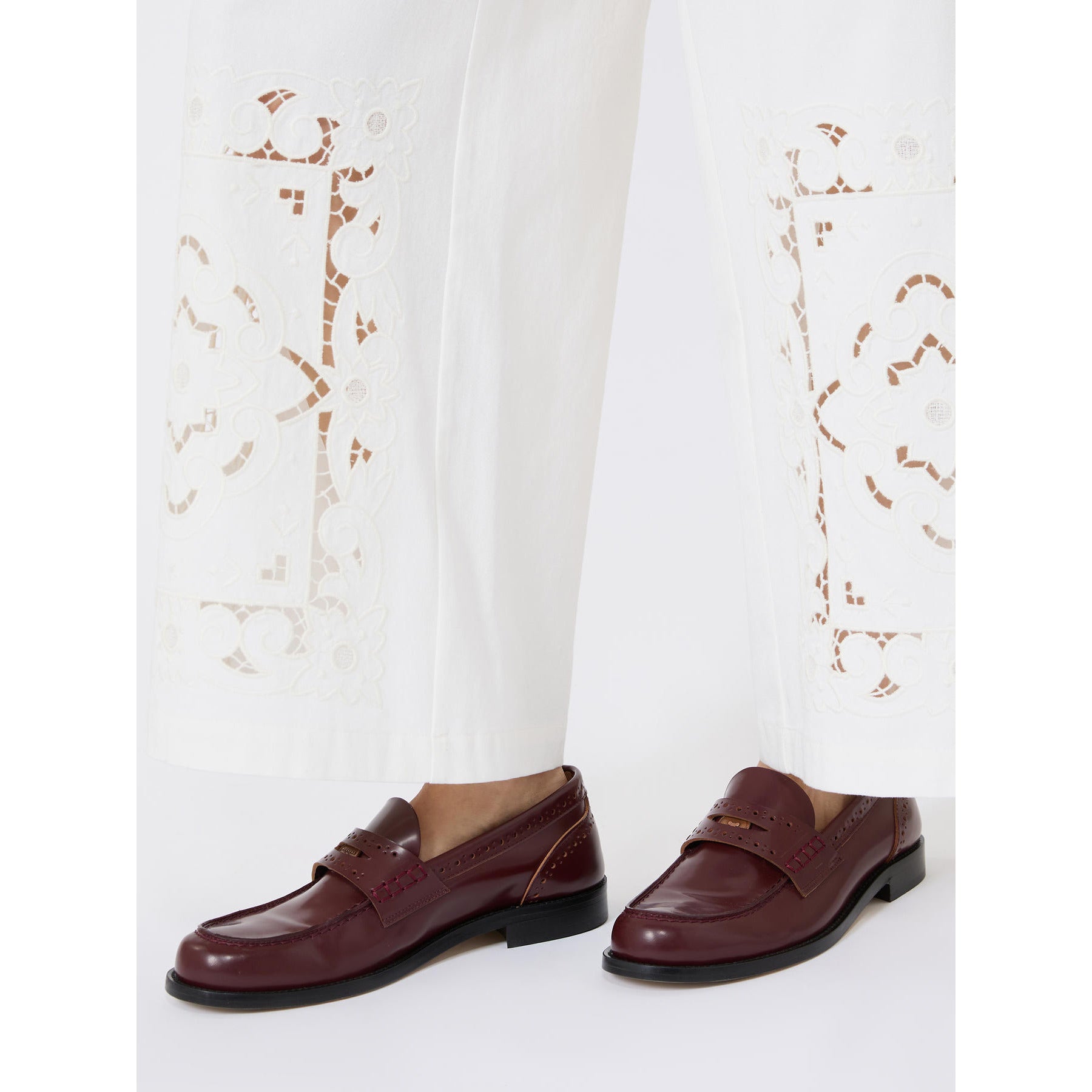 Brown loafers worn with white pants featuring floral embroidery on a white background