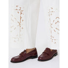 Brown loafers worn with white pants featuring floral embroidery on a white background