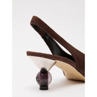 Brown high-heeled shoe with a small black bottle on a white background