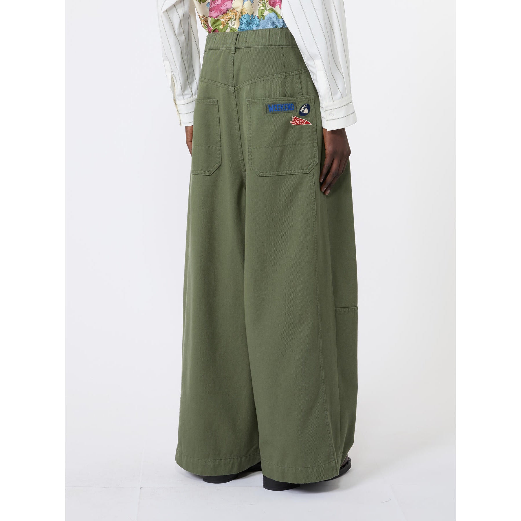 Person wearing green wide-leg pants with a brand logo on a white background