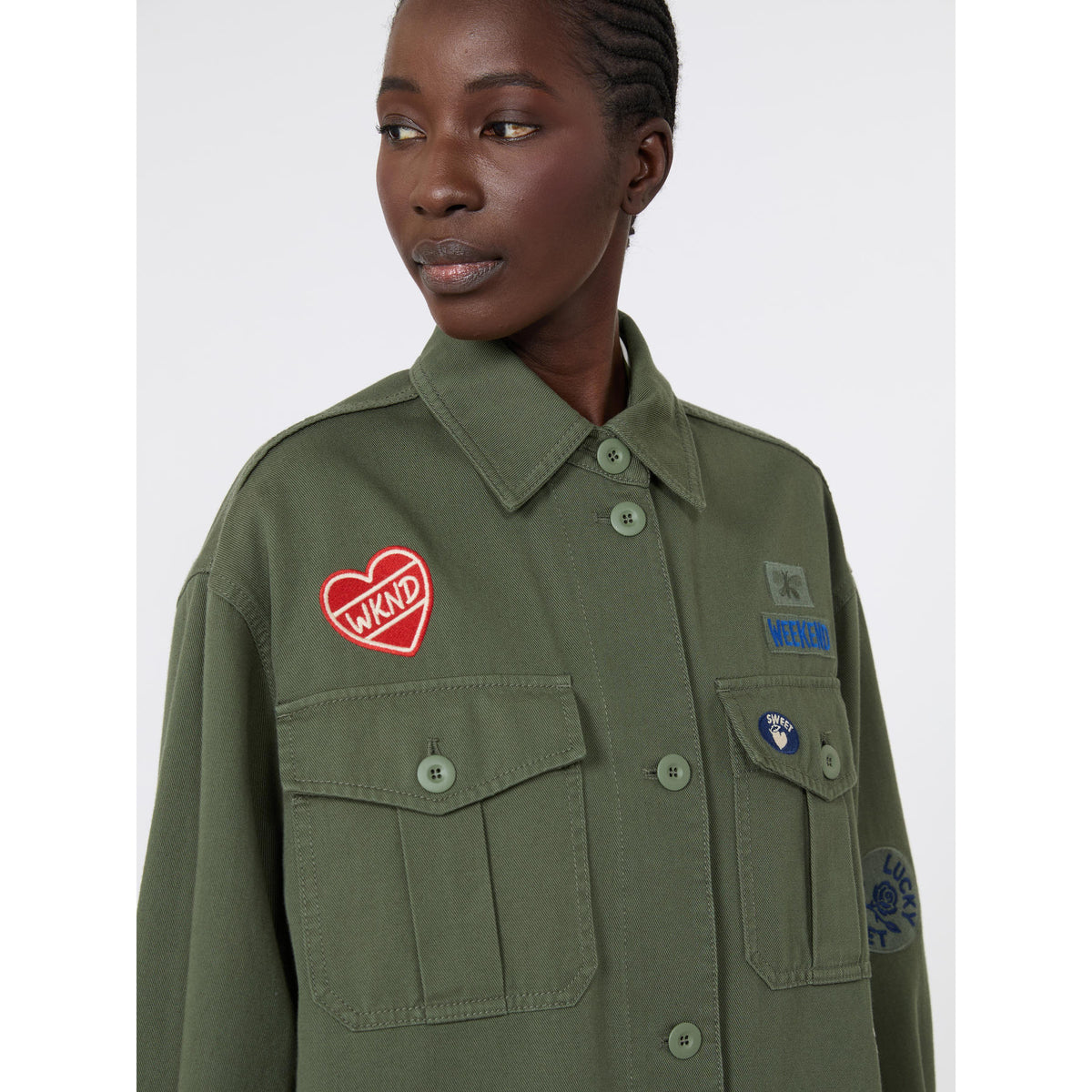 Person wearing a green jacket with patches on a white background