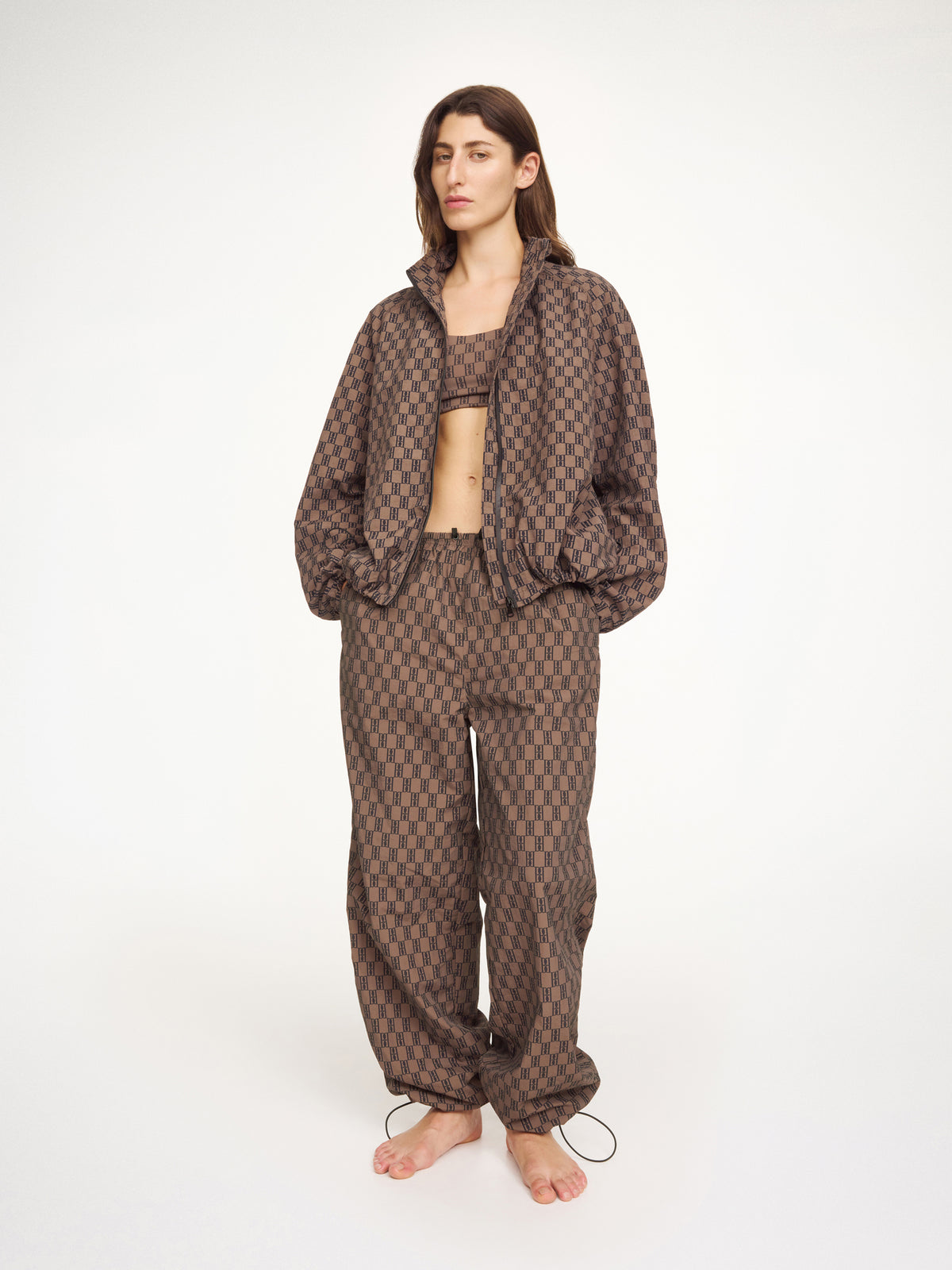 Person wearing a brown patterned anorak, bra and pants by Malene Birger on a white background
