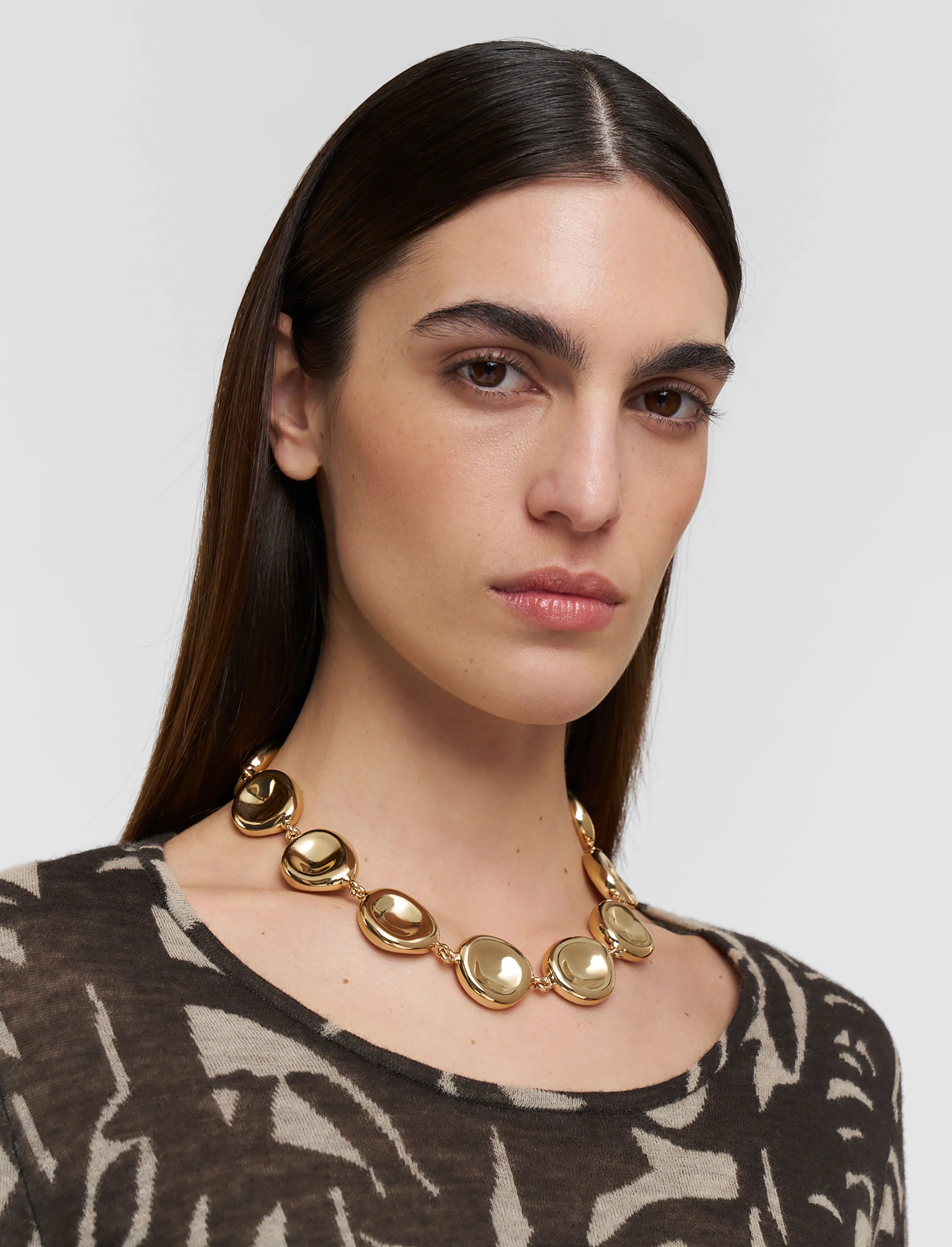 Woman wearing a gold necklace against a plain background