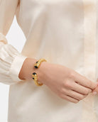 Gold bracelet with black stones on a person's wrist against a neutral background