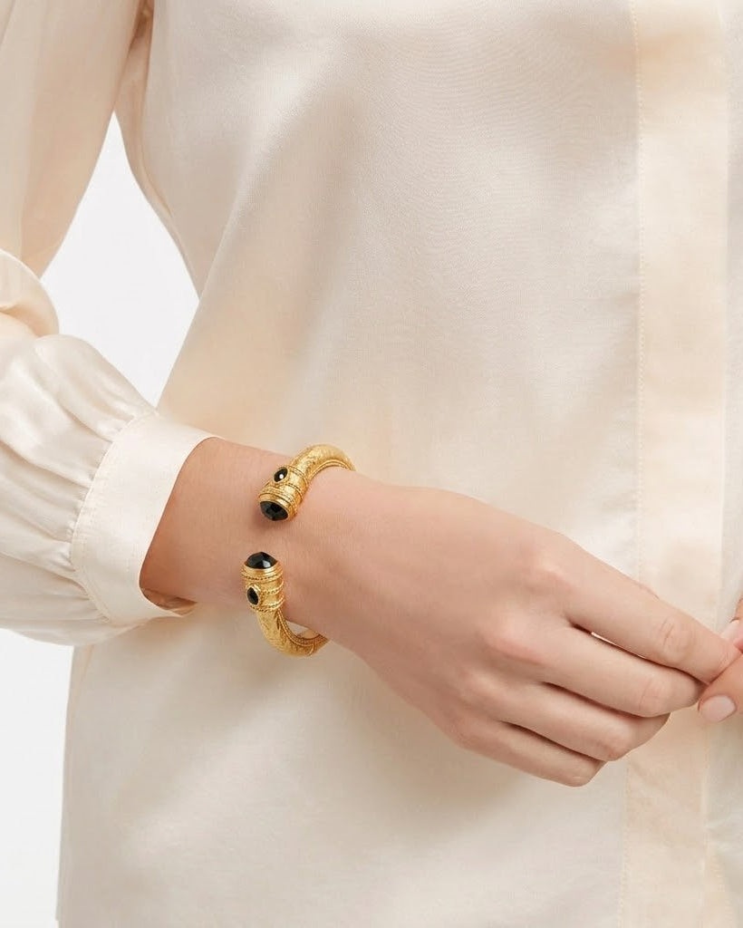 Gold bracelet with black stones on a person's wrist against a neutral background