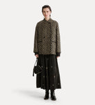 Person wearing a patterned jacket and black skirt on a white background