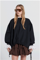 Person wearing a black oversized sweater with lace cuffs and a brown skirt on a white background