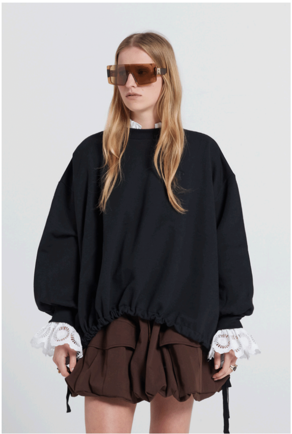 Person wearing a black oversized sweater with lace cuffs and a brown skirt on a white background